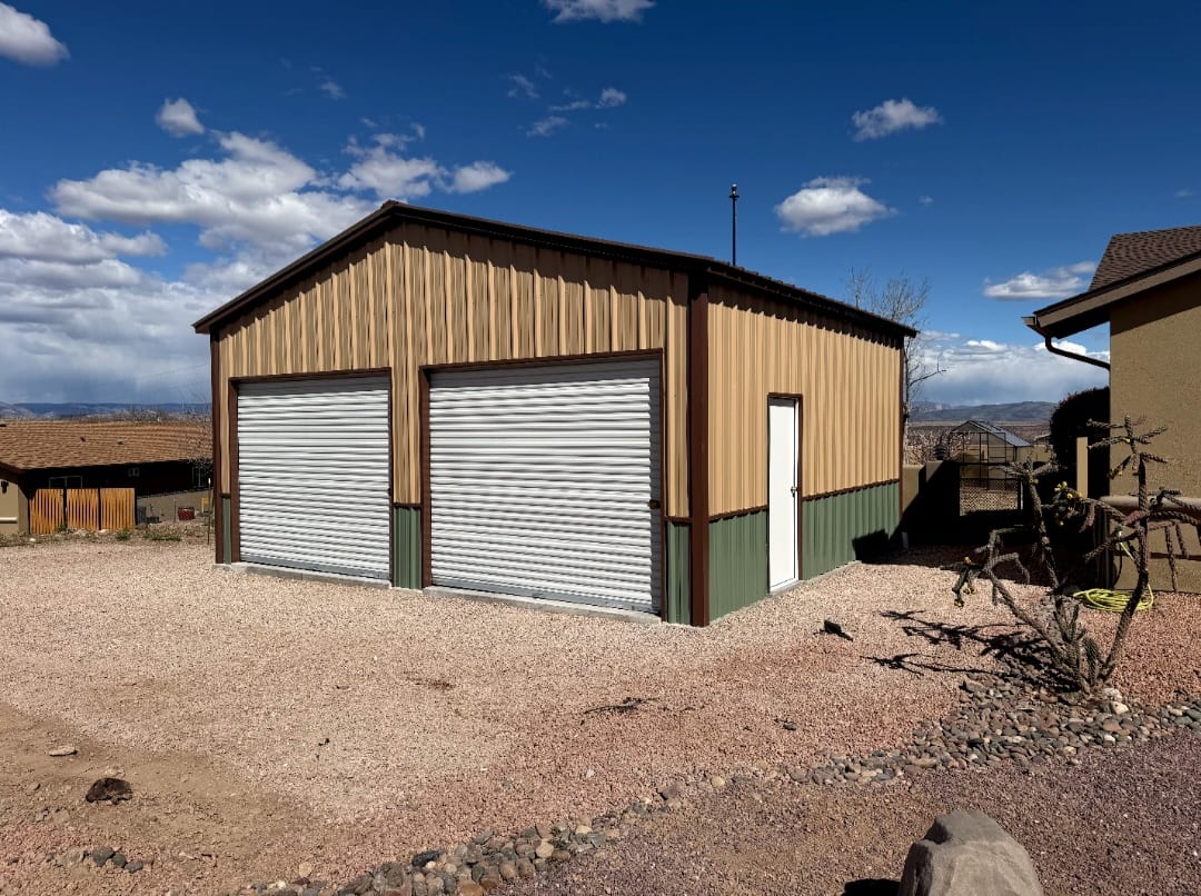 24 x 22 tan metal garage with green wainscot and two white roll-up doors on a gravel lot