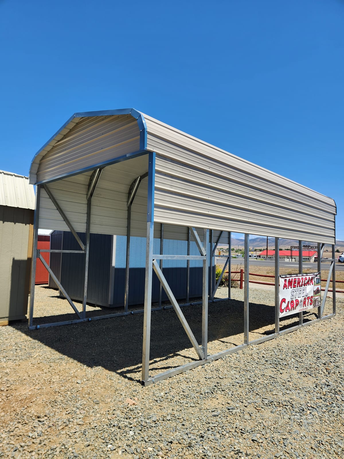 12 x 24 open metal carport with a white rounded roof and blue trim on gravel