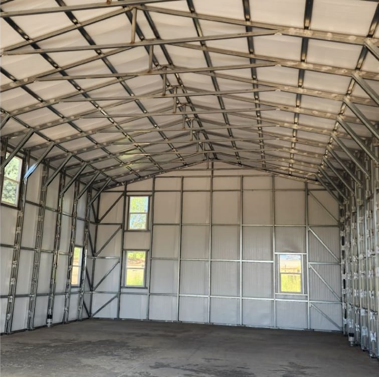 Inside a steel garage: exposed framing, white wall panels and three windows